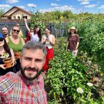 Șase oameni zâmbind într-o grădină de legume, unul dintre ei ține un ghiveci