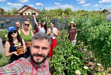 Șase oameni zâmbind într-o grădină de legume, unul dintre ei ține un ghiveci