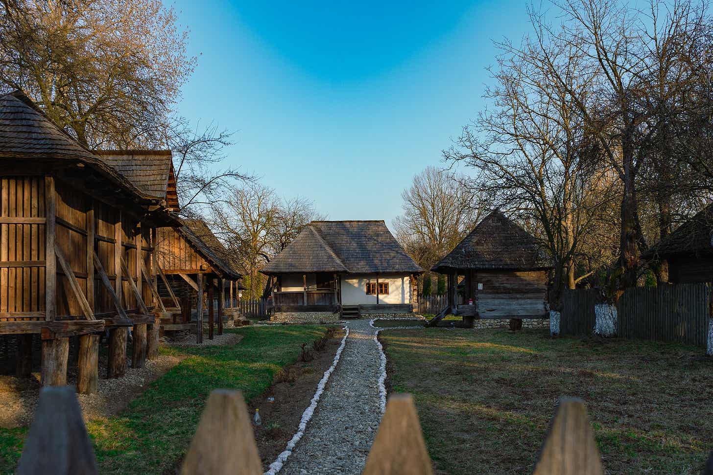 Alee printre case de lemn cu prispă, într-un muzeu în aer liber, primăvara devreme