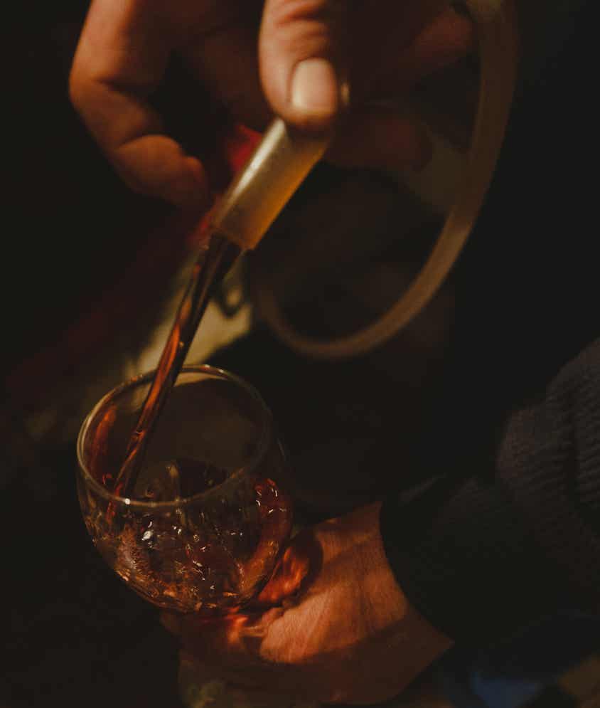 Vin roșu turnat dintr-o pipetă de cramă într-un pahar, ținut în mână