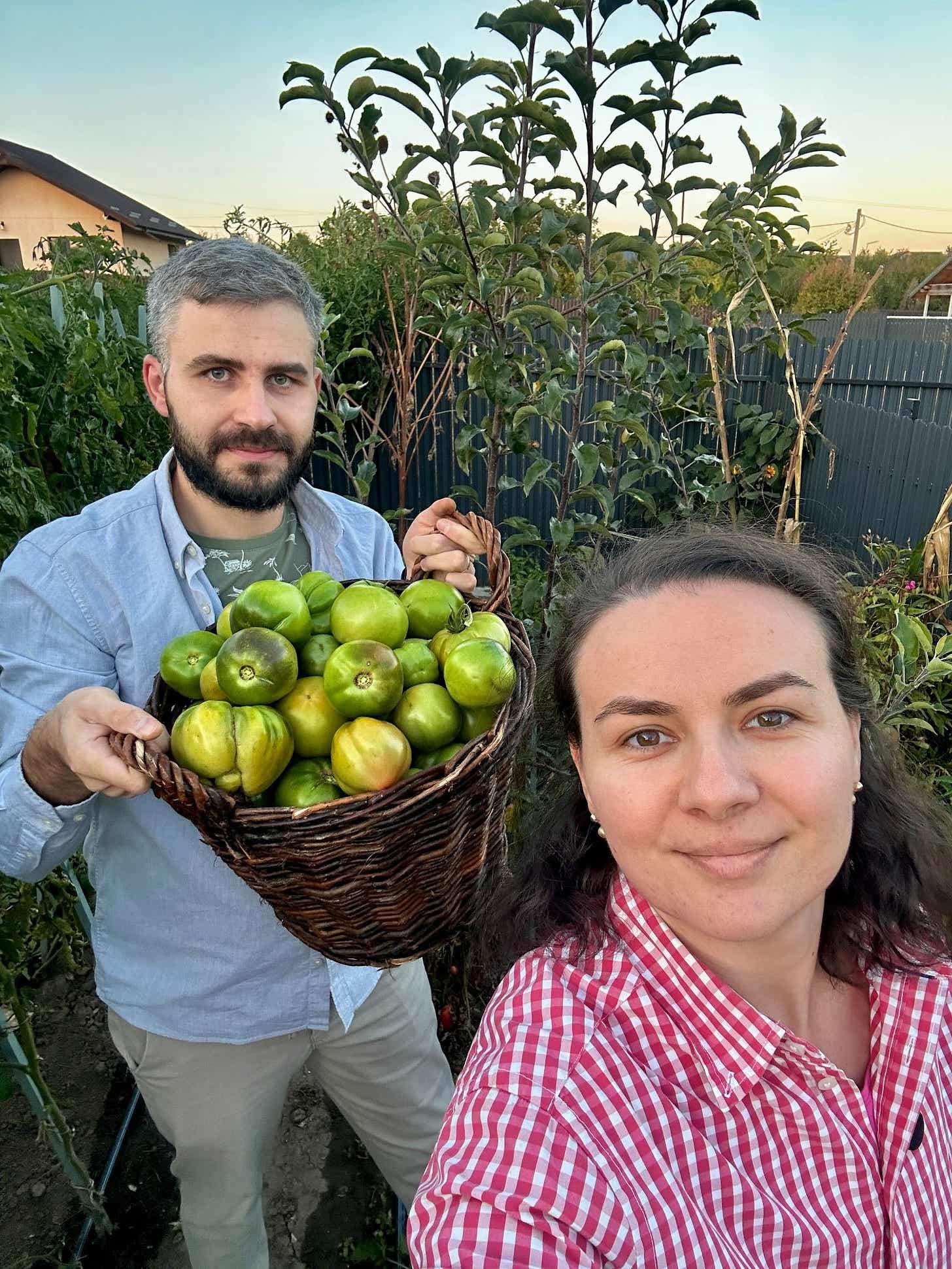 Ionuț Teoderașcu ține un coș de nuiele plin cu gogonele, lângă Nicoleta Felea, în grădina lor la asfințit