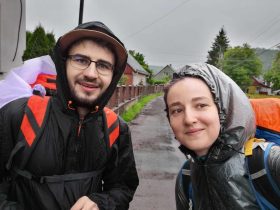 Ionuț Teoderașcu și jurnalista Anca Iosif, în pelerine de ploaie și cu rucsacuri, fac un selfie pe un drum ud de sat