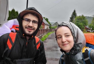 Ionuț Teoderașcu și jurnalista Anca Iosif, în pelerine de ploaie și cu rucsacuri, fac un selfie pe un drum ud de sat